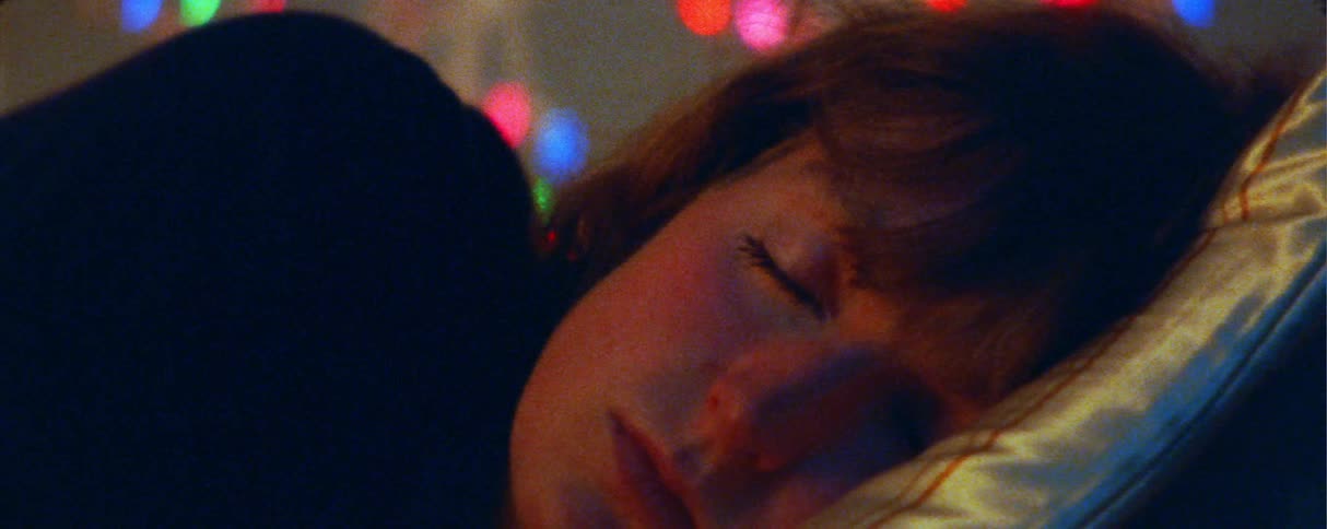 A woman lies in bed and slowly opens her eyes as she wakes up her face captured in a closeup against a blurred background of colorful decorative lights