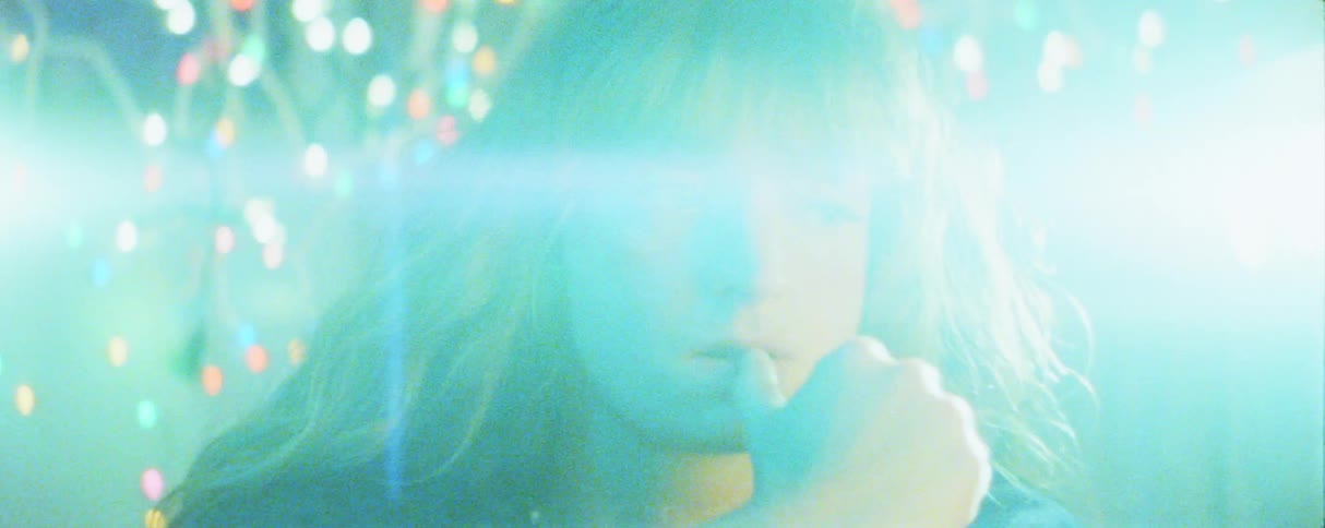 A woman with long hair stares forward pensively while biting her thumb in a room filled with blue light anamorphic lens flares and soft background bokeh