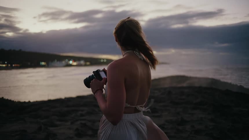 Woman with a camera on a rock with waves crashing against it
