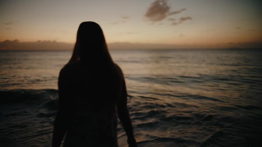 Woman walking along the coast as waves roll in to shore