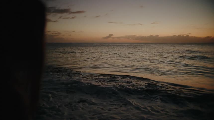 Silhouette of a person moving to the the left and right at a beach next to the sea outdoors during dusk or dawn