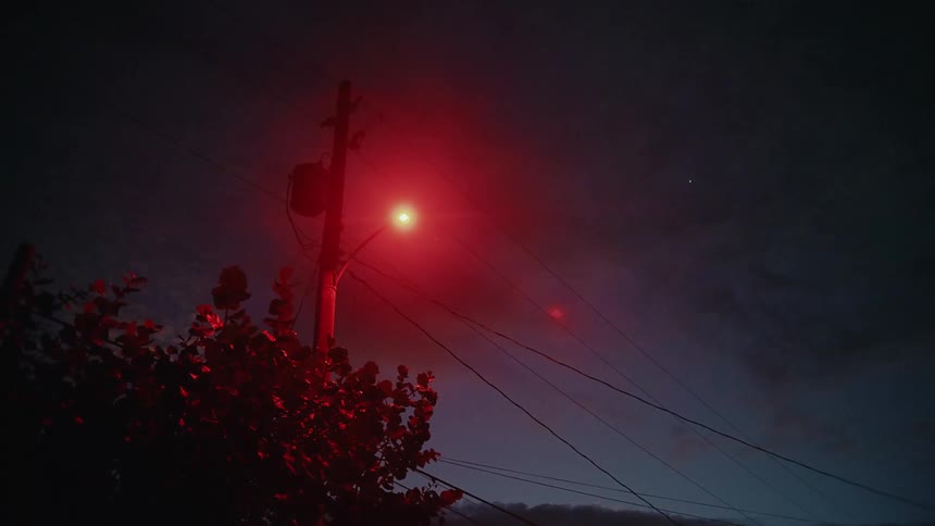 There are the thin dark power lines that stretch diagonally across the night sky they intersect near a wooden utility pole creating a geometric web against the dark cloudsthere is a distinct vertical line formed by the utility pole itself this pole s