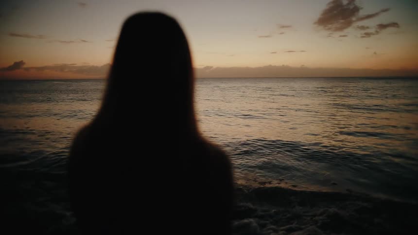 Sunlight shines on rippling waves as a woman walks along the coast