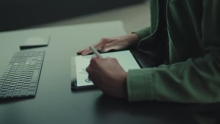 Young adult man with a beard drawing on a tablet over a desk indoors