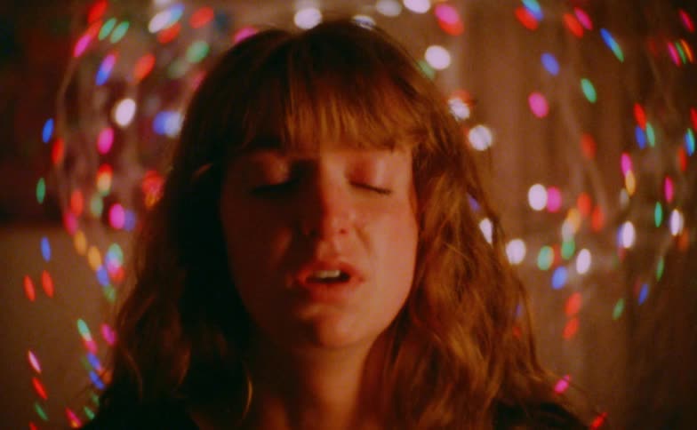 Visibly distressed with a tear in her eye a young woman closes her eyes surrounded by a swirl of colorful blurred lights