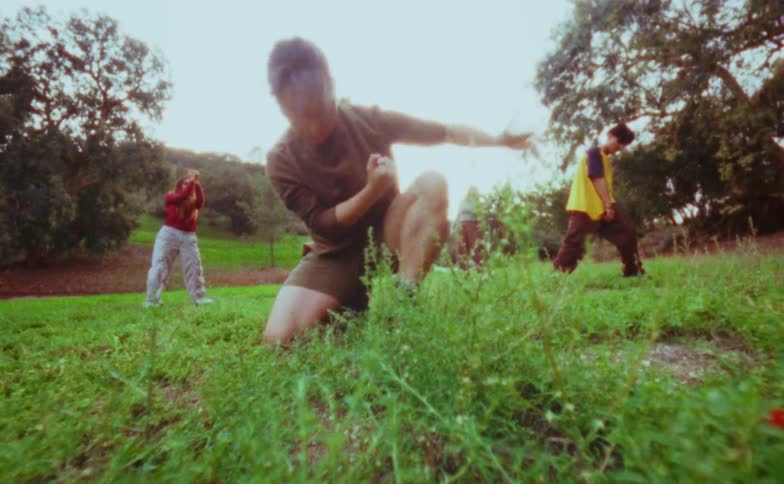 Three people practice martial arts on a grassland at midday two young women and one young man moving in coordinated stances under the bright sun