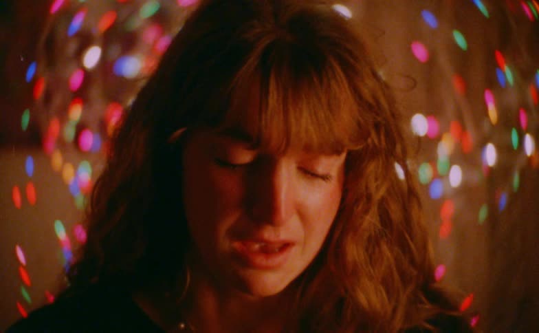 Person cries in closeup with warm lighting and defocused colorful light points in the background