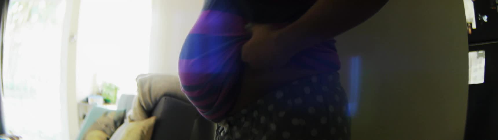 Woman inside house pulling shirt down over her pregnant stomach