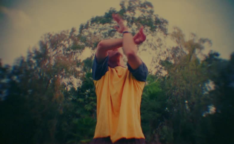 Teen boy performing dance moves outdoors next to a grove