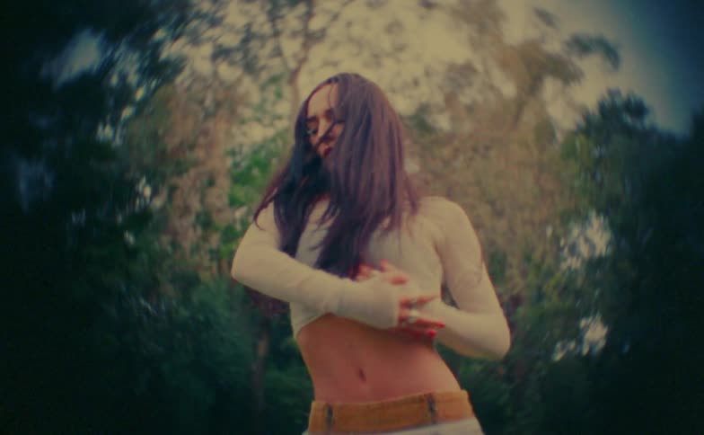 Woman performs dance movements with hands over the torso in an outdoor wooded setting