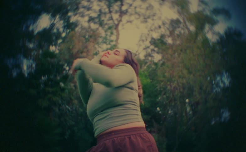 Teenager girl making dance moves in front of trees outdoors during day time