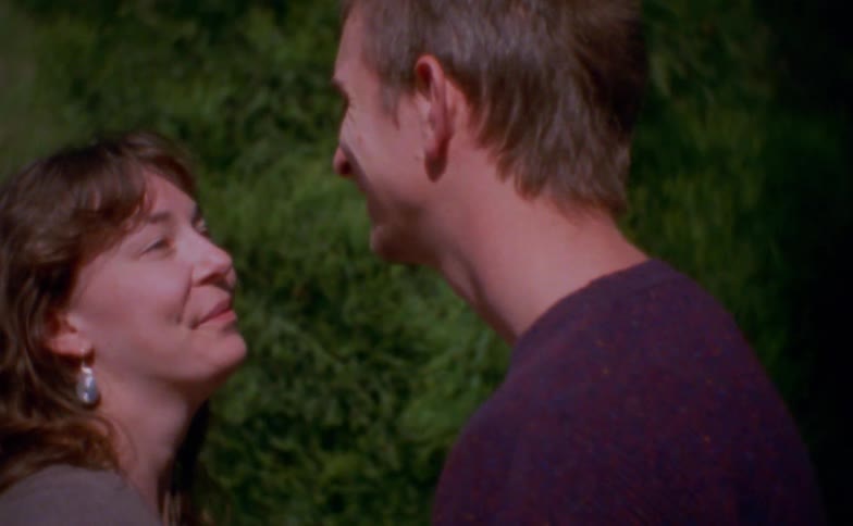 A young couple stands outdoors near a tree happily talking together in the warm daylight