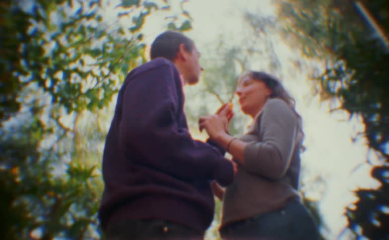 The man and woman are facing each otherthe woman feeds the man something and then she kisses him