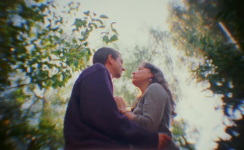 Couple stands very close beneath trees with soft natural light around them