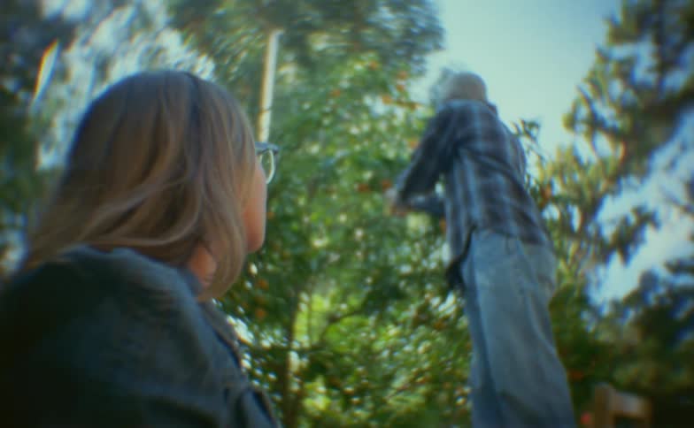 With a dreamy distorted lens effect a young woman watches as a man picks fruit from a tree