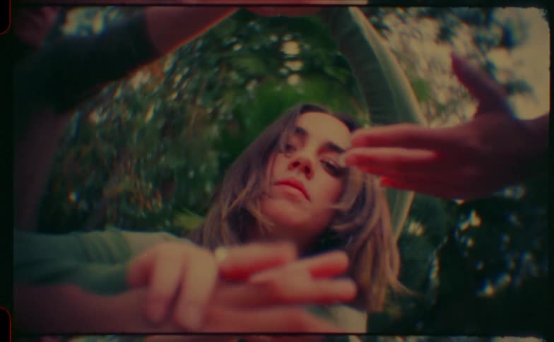 Woman performs dance movements with raised arms in an outdoor wooded setting