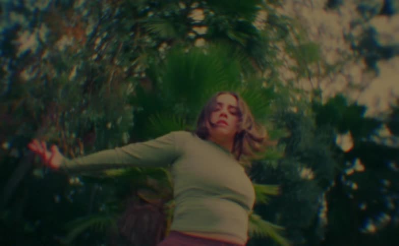 A woman dances gracefully with flowing movements amid lush greenery in soft daylight