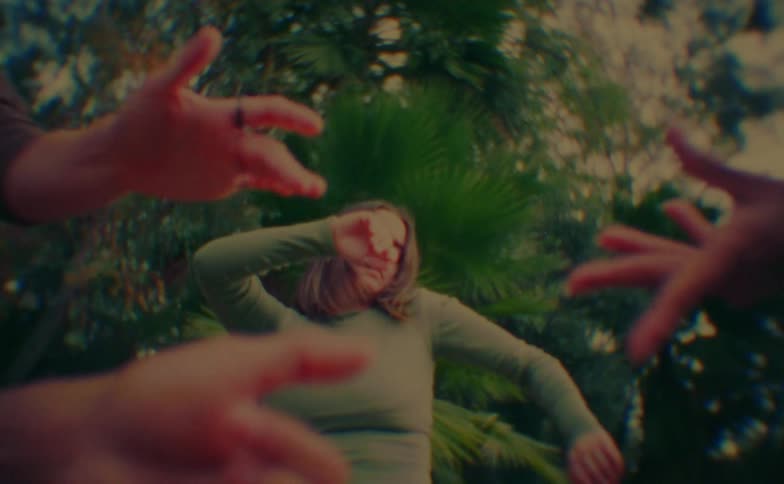 Teenger girl dancing around the hands of other dancers with trees on the background outdoors