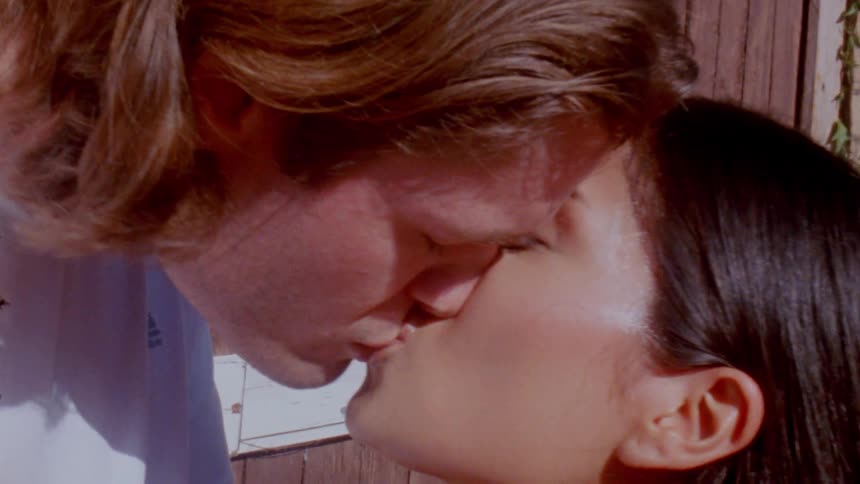 A young couple shares a passionate kiss outdoors under the bright midday sun