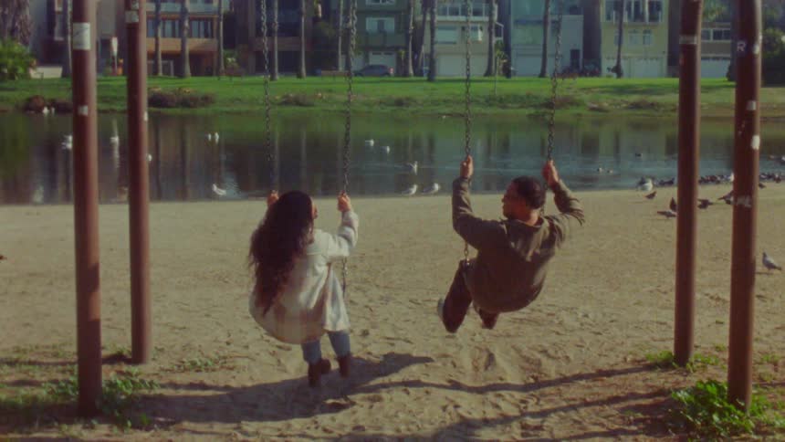 Couple uses swings in a park by an urban lake during daylight