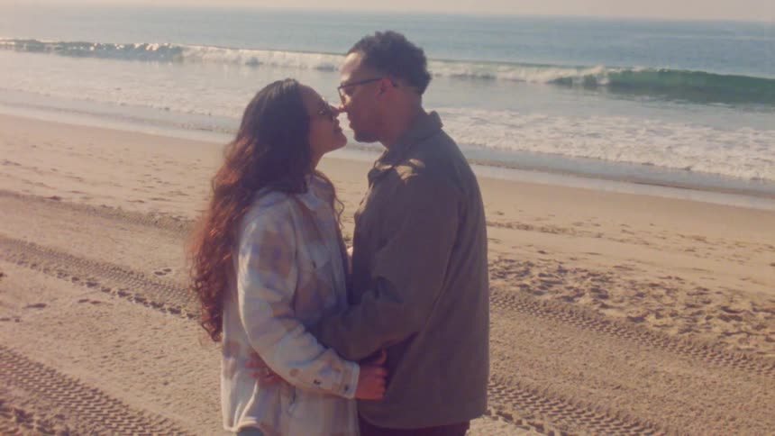 Man and woman standing together on the beach and kiss as waves roll in to shore