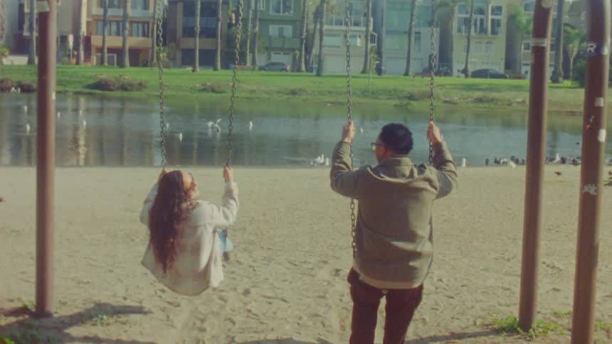 Couple uses swings in a park by an urban lake during daylight