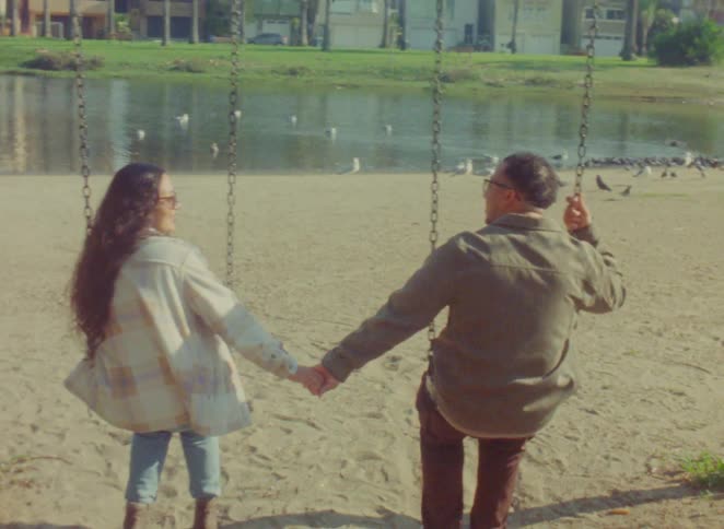 Couple holding hands in a park with swings and a lake in the background