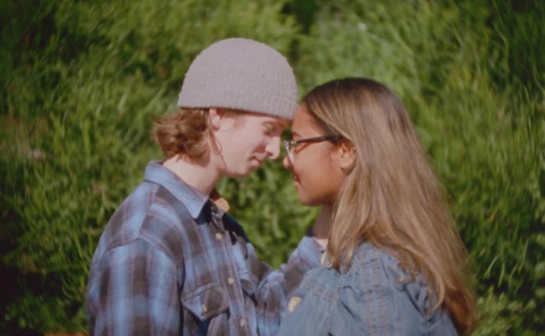 Adult people stand face to face with light physical contact in an outdoor setting with greenery in the background
