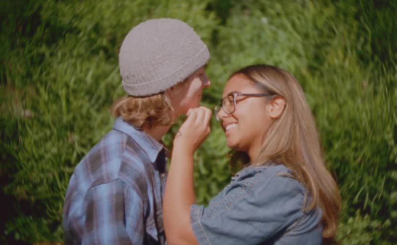 Couple interacts closely outdoors with greenery in the background under natural light