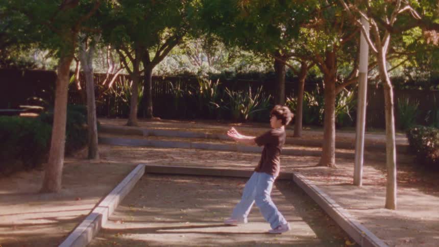 A young boy dances energetically in a backyard at midday showing off his moves under the bright sun