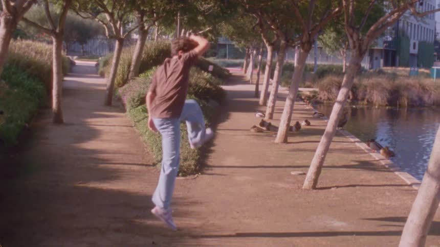 The boy is spinning and dancing by the trees and bushes