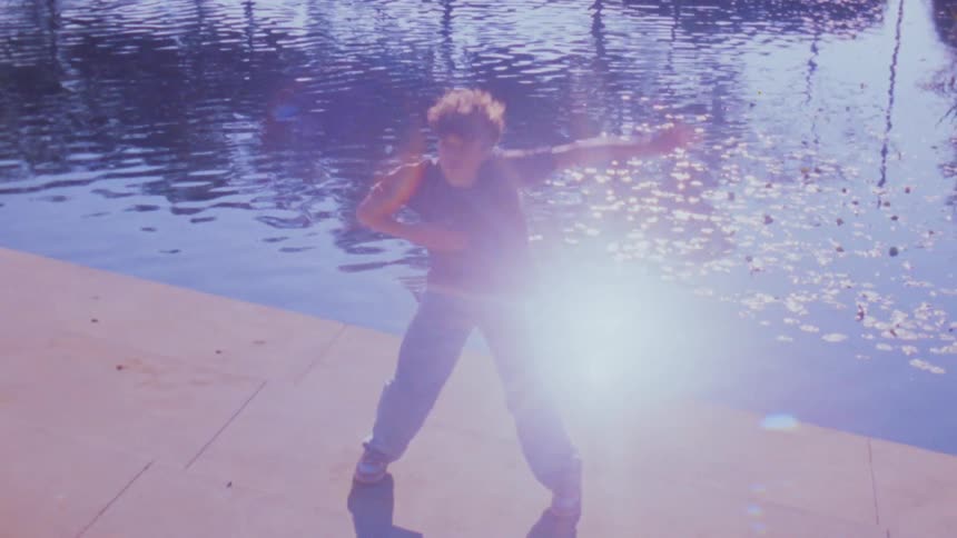 A teenage male dancer dancing by a pond outdoors during daytime