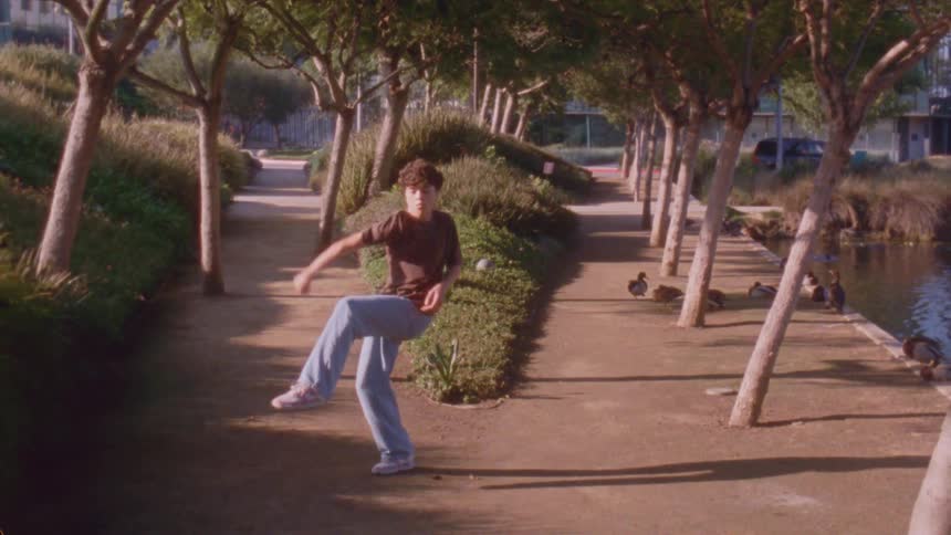 Person performs dance movements on a treelined path in an urban park during daylight