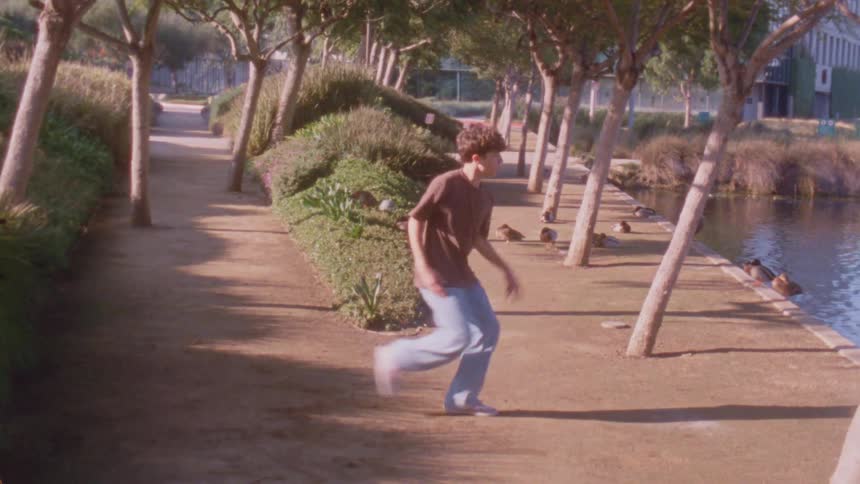 A teenage male dancer dancing outdoors on a walkway beside a pond during daytime