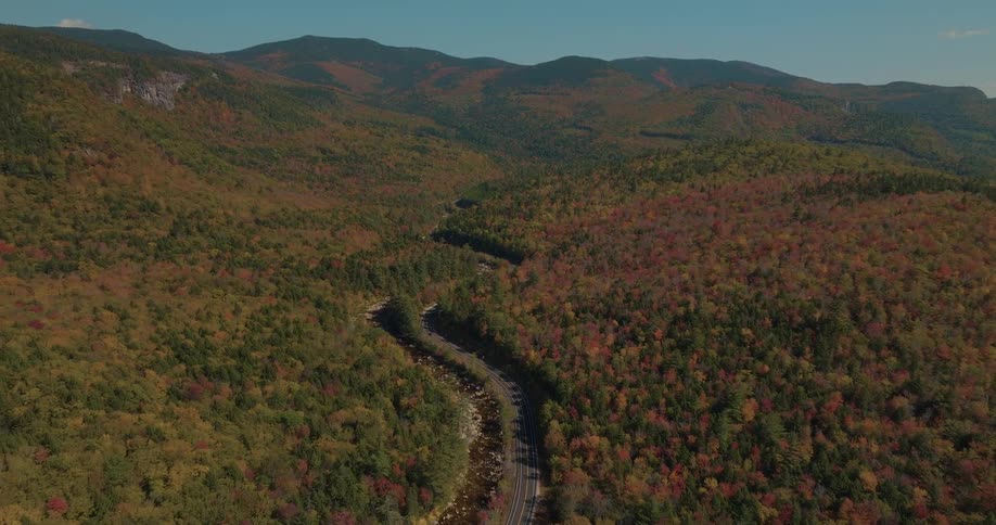 Light traffic moves on a highway through forested mountains with trees in bright fall colors