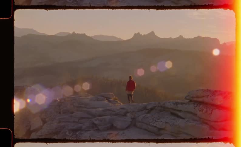 Person stands on a rocky formation observing mountains under golden sunset light