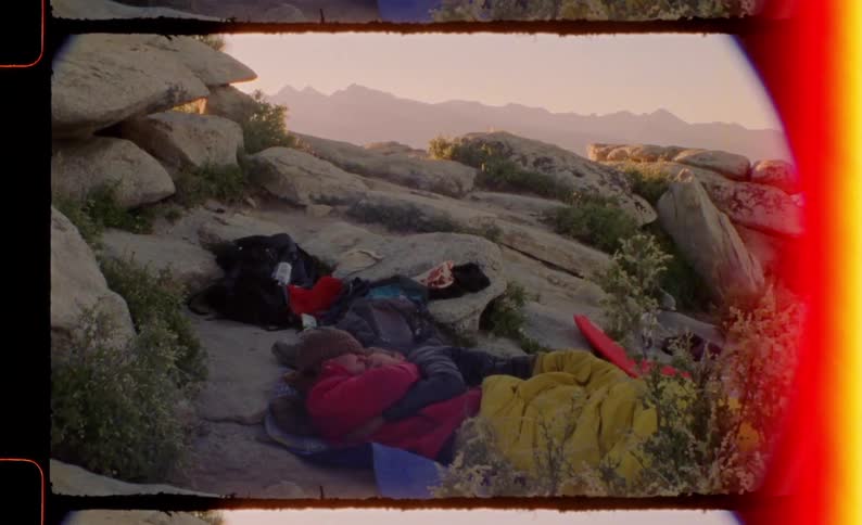 People lying in sleeping bags on rocks in a natural environment at dawn