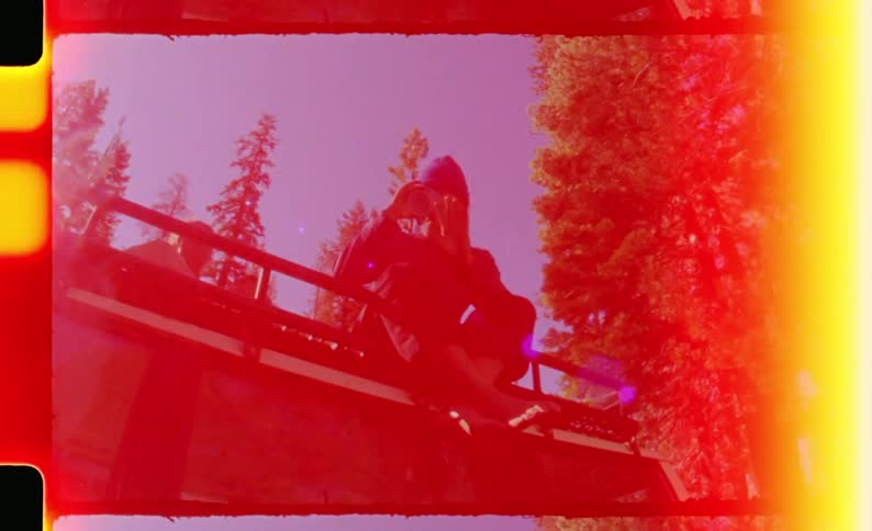 Two teenagers sit on a bridge in the woods at midday with one of them drinking from a can as sunlight filters through the trees around them