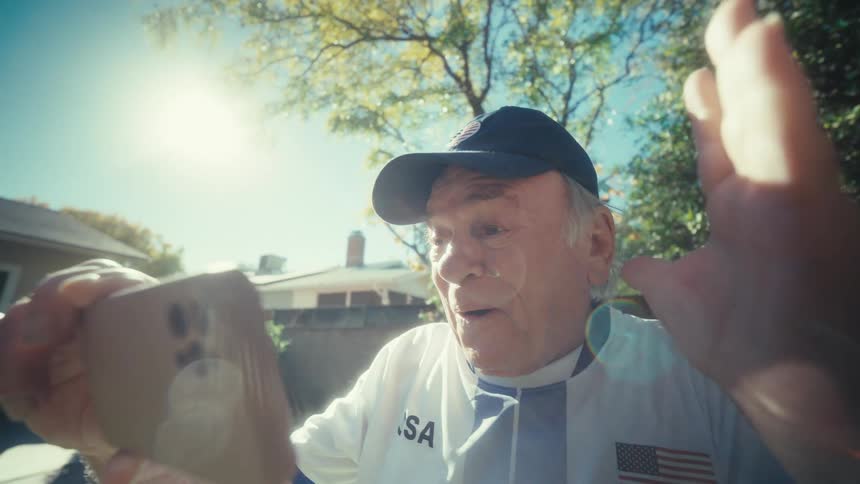 A senior man excitedly reacts while watching sports on his smartphone in a sunny backyard