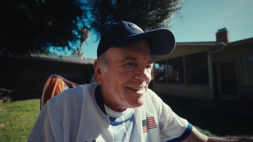 Elderly man sat in the yard holding and watching a smartphone