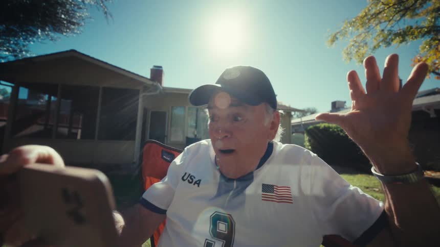 Elderly man sits in the backyard with a happy expression watching something on his smartphone