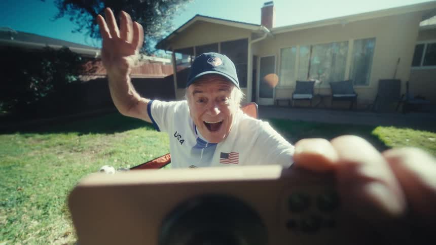 Elderly man in a cap beaming happily watching on his smartphone