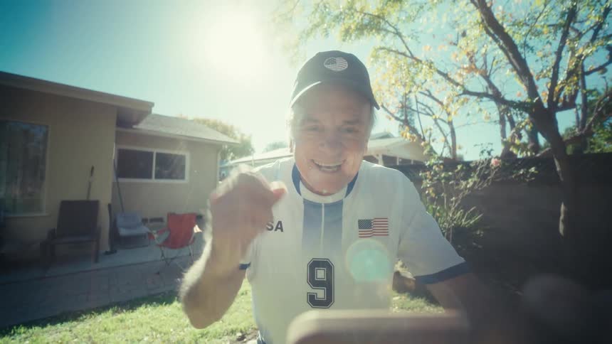 Elderly man standing in the yard watching something on his smartphone