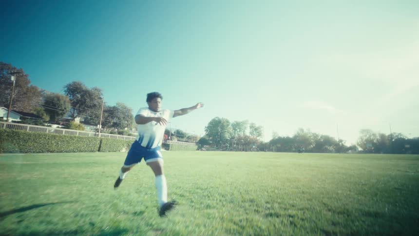 An athlete powerfully kicks a soccer ball across a sunlit field