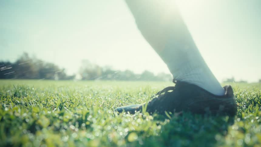 Person wearing soccer cleats running with a soccer ball on a field