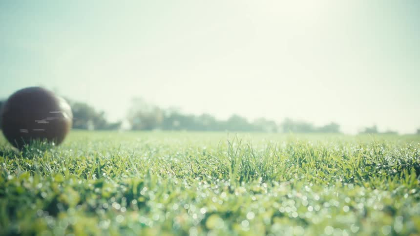 Person wearing soccer cleats pushing a leather ball on a grass soccer field