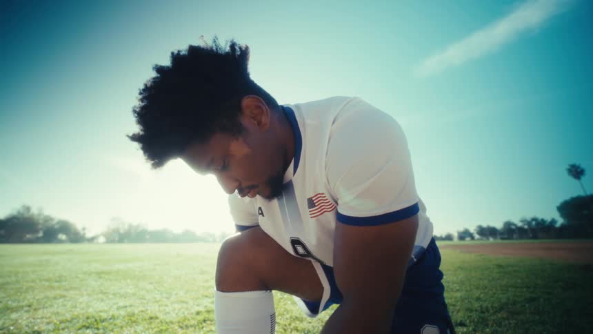 Man ties his shoe while in a field before staring ahead on a sunny summer day