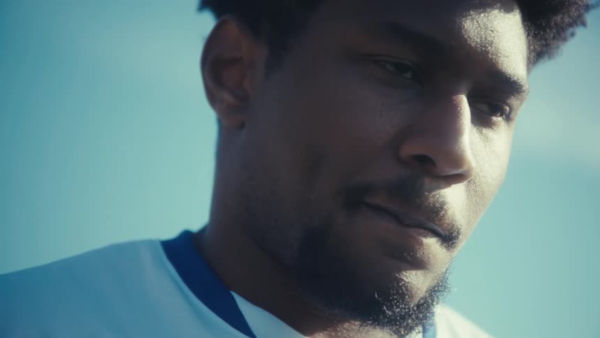 A man wearing a white usa soccer jersey with the number nine looks down while standing on a grassy field under a clear blue sky on a bright day