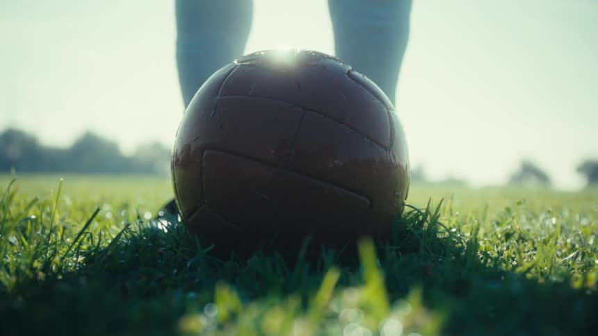 Person resting their foot on a leather soccer ball on the grass