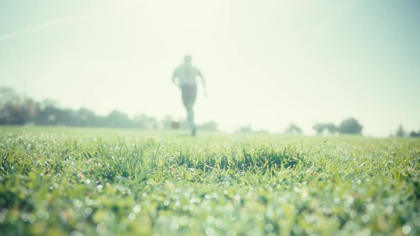 Soccer ball sits on the grass in a field as a player steps over and kicks the ball away